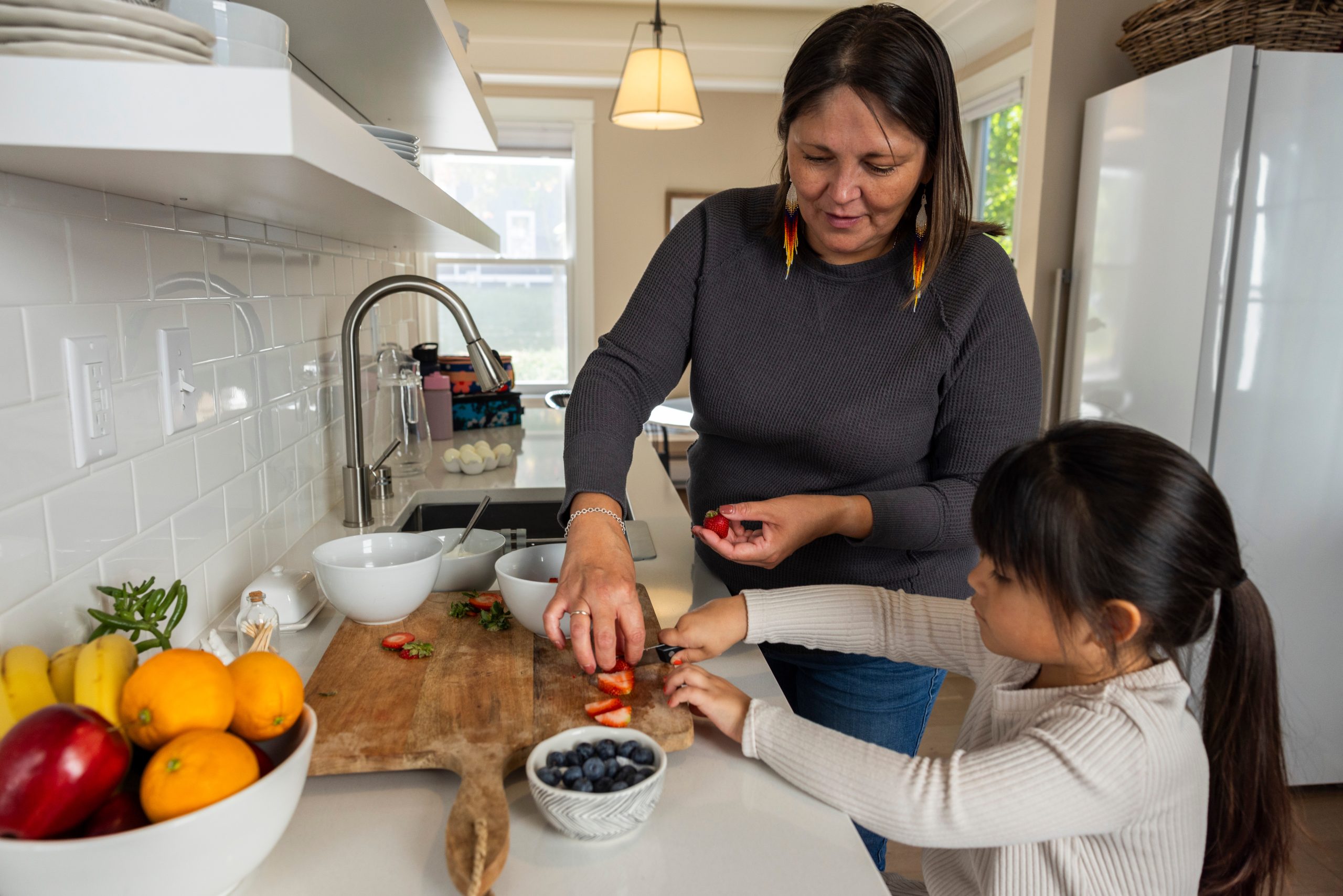 Ojibwe mother and daughter cut strawberries on cutting board